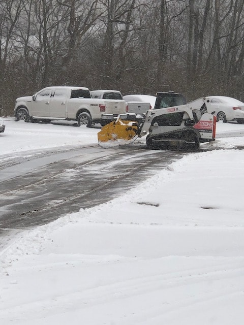 Skid steer plow clearing a snowy parking lot